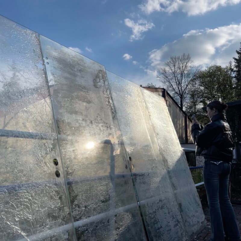 Große bearbeitete Glasscheiben im Außenraum, in denen sich Licht, Himmel und Umgebung spiegeln