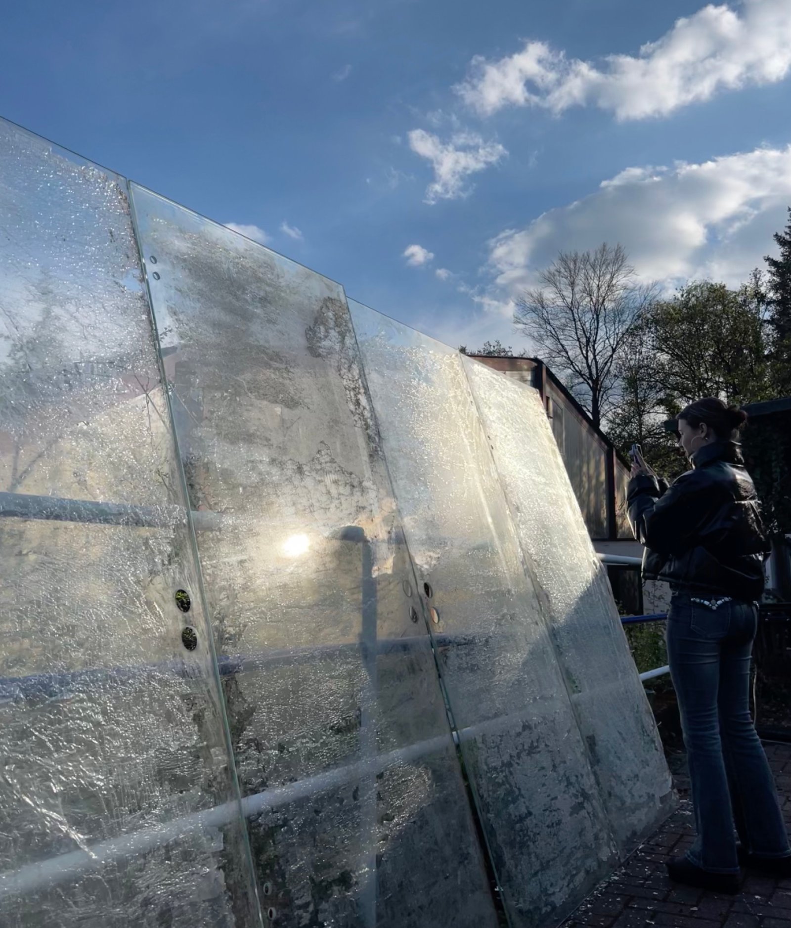 Große bearbeitete Glasscheiben im Außenraum, in denen sich Licht, Himmel und Umgebung spiegeln